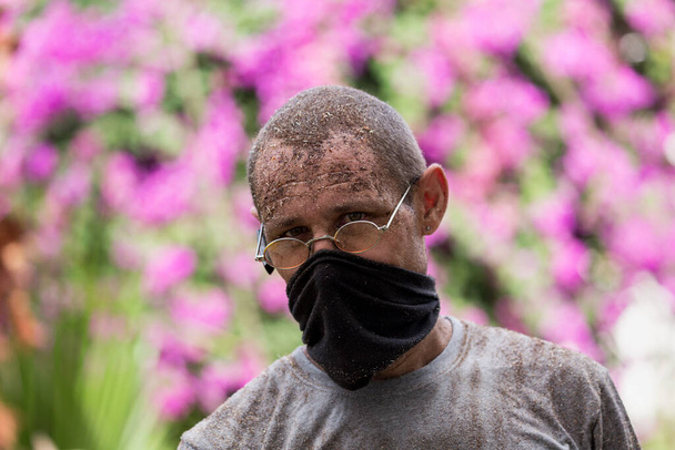 Άνθρωπος με γυαλιά και μαύρη μάσκα. Είναι κουρασμένος και βρώμικος από τη σκόνη μετά από σκληρή δουλειά στον κήπο, το πρόσωπο και τα ρούχα είναι βρώμικα. Έννοια σκληρή δουλειά, γεωργία, κηπουρική ή οικολογία. Επιλεκτική εστίαση - Φωτογραφία, εικόνα