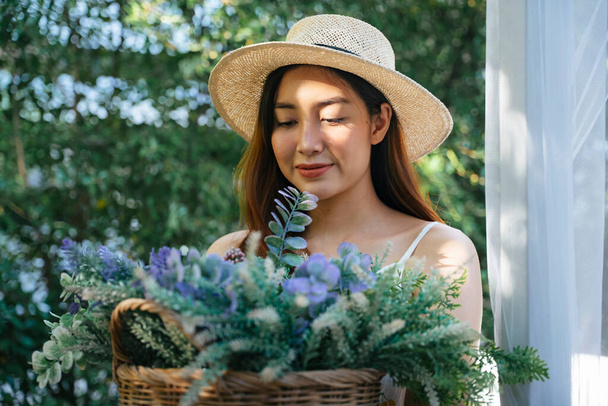 Portret van jonge aziatische vrouw met bloemmand zittend in de tuin. - Foto, afbeelding