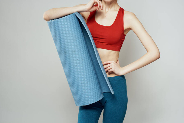 Woman holds in hand a mat for fitness sport slim figure exercises light background - Fotoğraf, Görsel