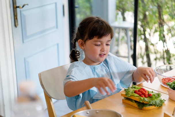 Allegro bambino asiatico godere di mangiare sandwich vegetale per la prima colazione a casa. - Foto, immagini