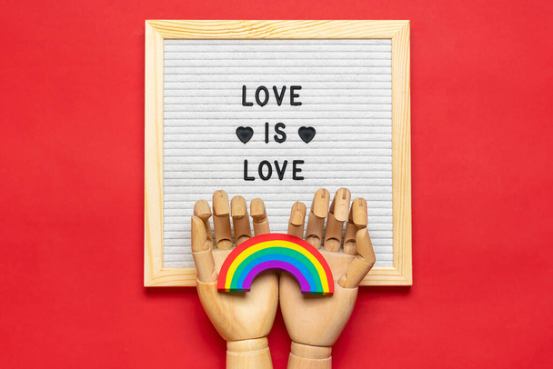 Plstěná deska s uvozovkou, dřevěné ruce drží duhu s barvami LGBT izolované na červeném pozadí Top view Flat lay Pýcha měsíc koncept - Fotografie, Obrázek
