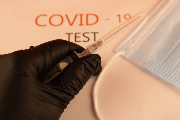 A hand in a black glove with a syringe on a background of a white form with the inscription "test covid-19" - Valokuva, kuva