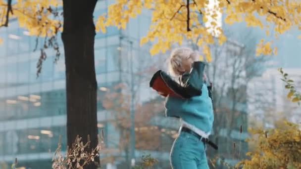 Nuori onnellinen valkoihoinen nainen nahkatakissa hyppii ja pyörii puistossa syyspäivänä - Materiaali, video