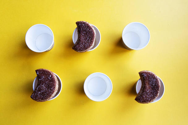 Μια σειρά από semilunar ζαχαρωμένα μπισκότα και κούπες από χαρτόνι που διοργανώνονται σε ένα φωτεινό κίτρινο φόντο - Φωτογραφία, εικόνα