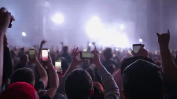 As pessoas em um concerto de música gravam o desempenho da banda em seus smartphones. Atmosfera de clube e mãos levantadas com telefones. Visão traseira. O conceito de entretenimento - Filmagem, Vídeo