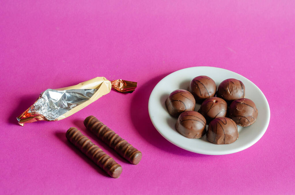 Chocolate candies in white saucer on pink background. Serving of Pastry among crumpled random candy wrappers. Sweet treats. Selective focus. - Fotó, kép