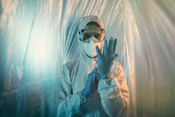 Foto eines Mannes in voller Sicherheitskleidung hinter Plastikvorhang - Foto, Bild