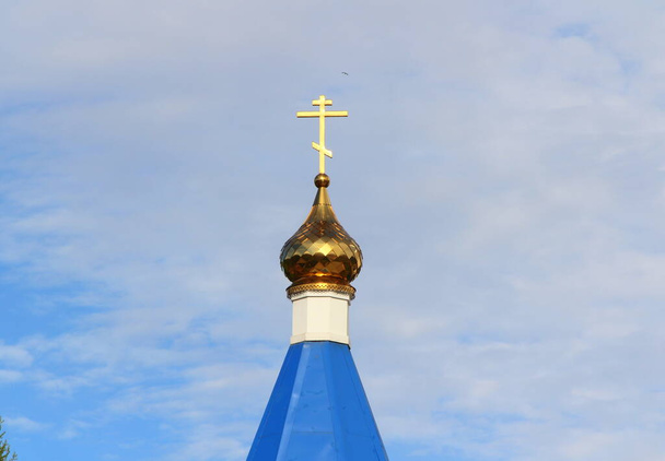 Orthodox Christian church with blue roof, golden dome and cross in Russia. A building for religious ceremonies with a bell tower against a cloudy sky. - Foto, Bild