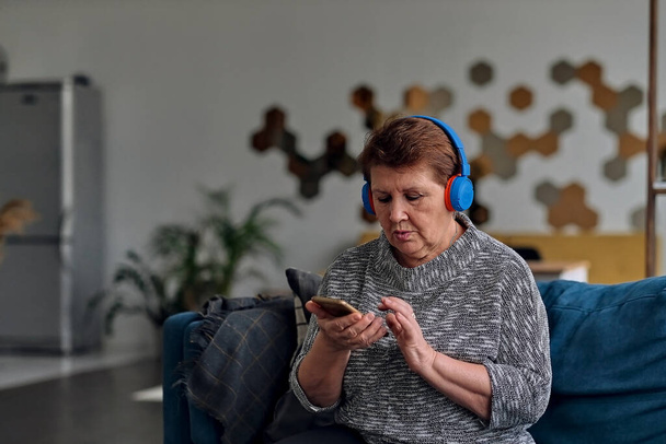 New life of favorite book. Senior woman enjoying audiobook in headphones, free space. - Photo, Image
