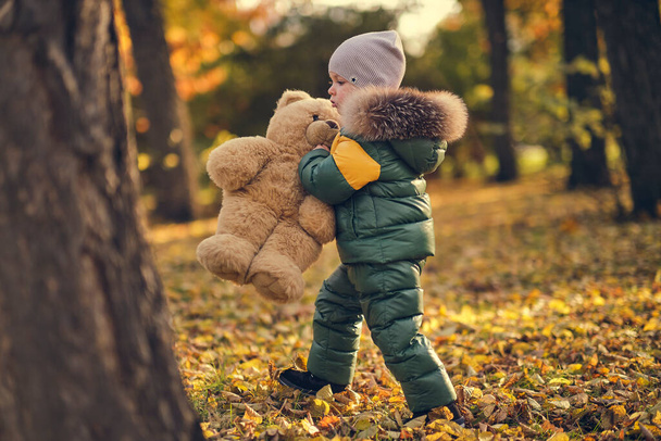 Słodki chłopczyk bawiący się na dworze. Szczęśliwe dziecko spacerujące w jesiennym parku. Mały chłopiec nosi modną kurtkę. Jesienna moda. Stylowe dziecko na zewnątrz. - Zdjęcie, obraz