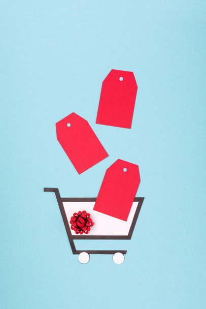 スーパー販売日またはシングル日の概念。青い紙の背景にショッピングトロリー、ギフトボックスと赤のタグ。中国のオンラインショッピング。トップビュー、フラットレイアウト、コピースペース. - 写真・画像