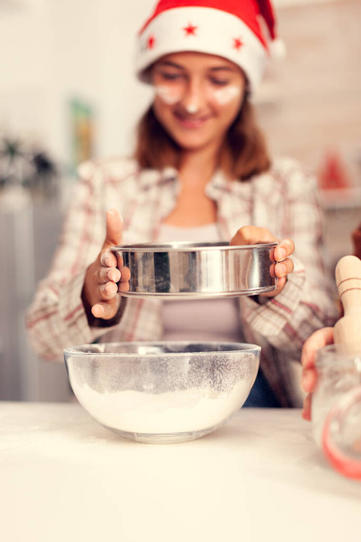 Girl sifts flour through a sieve on christmas day - Photo, Image