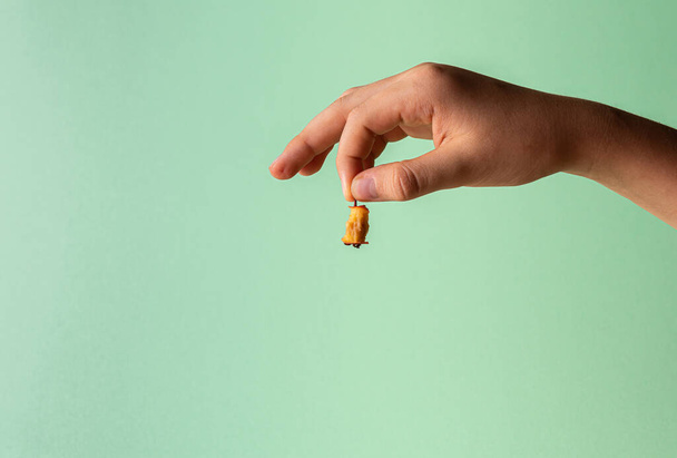 Hand of Caucasian teenager boy with haw stump in fingers. Small fruit leftovers in human hand. Copy space. Unrecognizable person. Horizontal orientation. Healthy eating concept. Green mint background. - Photo, Image
