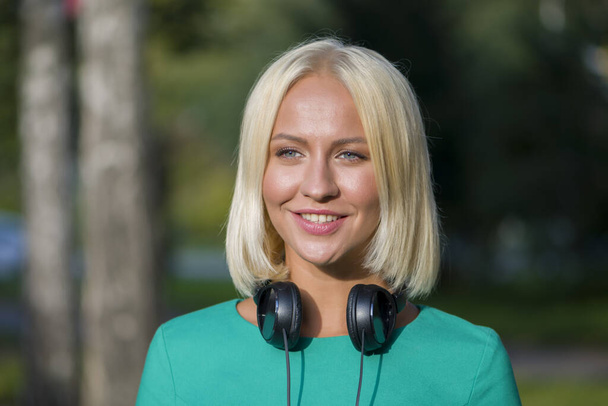 Schöne junge Blondine 25-30 Jahre alt mit Kopfhörern auf dem Hintergrund der Natur. - Foto, Bild