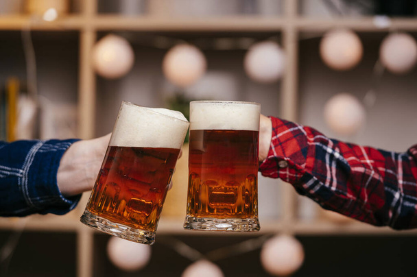 Two mugs full of beer drink in hands of two males. - Фото, зображення