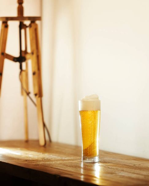 Copo de cerveja na mesa de madeira com macho em primeiro plano, foco no vidro. - Foto, Imagem