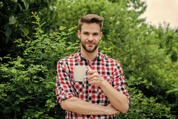 good morning. fresh inspiration and energetic beverage. handsome bearded guy drinking tea outdoor. he loves cocoa. food and drink. cheerful man in checkered shirt drink morning coffee - Zdjęcie, obraz