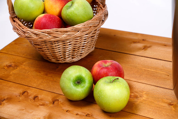 Image of red and green apples in wicker basket on wooden board - Foto, Imagem