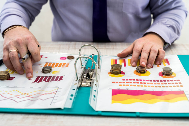 オフィスのビジネスマンは、コインを使用してチャートや文書を使用して会社の利益を分析します。事業分析と戦略の考え方 - 写真・画像