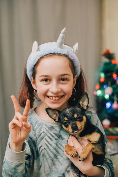 Adorable niña pequeña sosteniendo chihuahua cachorro de pie. chica sosteniendo perros chihuahua en sus brazos. niña de 9 o 10 años con una mascota en casa en sus brazos. El concepto de amor por los animales. - Foto, imagen