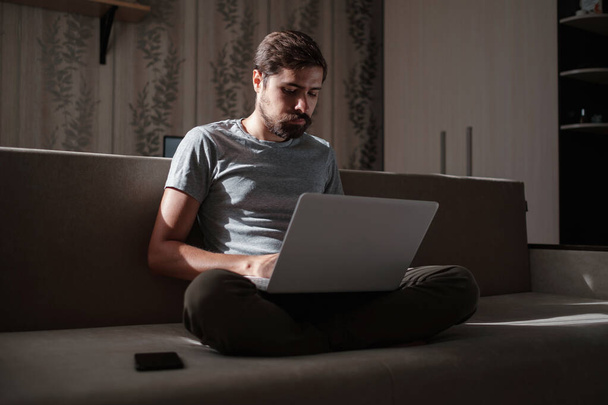 Vzdálená práce. Muž pracující na notebooku sedí na pohovce doma. Kopírovat mezeru pro text. hipster na volné noze pracuje z domova, studuje nebo komunikuje s partnery - Fotografie, Obrázek