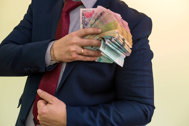 Человек в костюме держит в руках большую кучу украинских денег и показывает свой доход. UAH. новые банкноты 1000 и 500 гривен - Фото, изображение