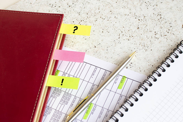 Um diário de negócios com abas coloridas com inscrições encontra-se em gráficos financeiros na mesa de escritório. - Foto, Imagem