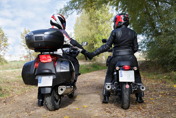 Motosikletlilerin üzerinde otururken el ele tutuşan iki motorcu. - Fotoğraf, Görsel