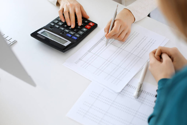 Accountant checking financial statement or counting by calculator income for tax form, hands close-up. Business woman sitting and working with colleague at the desk in office. Audit concept - Foto, immagini