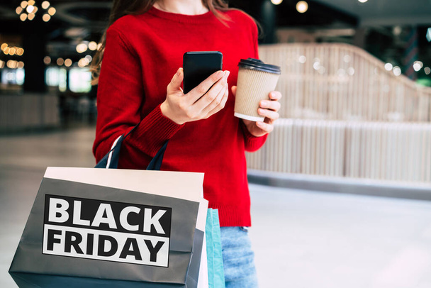 Beautiful trendy young woman with many colorful shopping bags in good mood with smart phone and credit card while walking in the mall during black friday - Foto, afbeelding