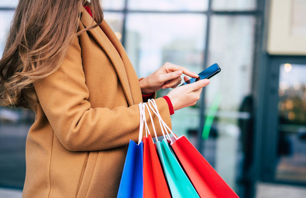 Beautiful trendy young woman with many colorful shopping bags in good mood with smart phone and credit card while walking in the mall during black friday - Foto, immagini