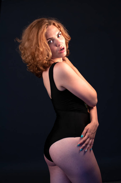 Beautiful seductive young red hair woman wearing bodysuit in studio. Dark background. Natural body. Without retouch - Φωτογραφία, εικόνα