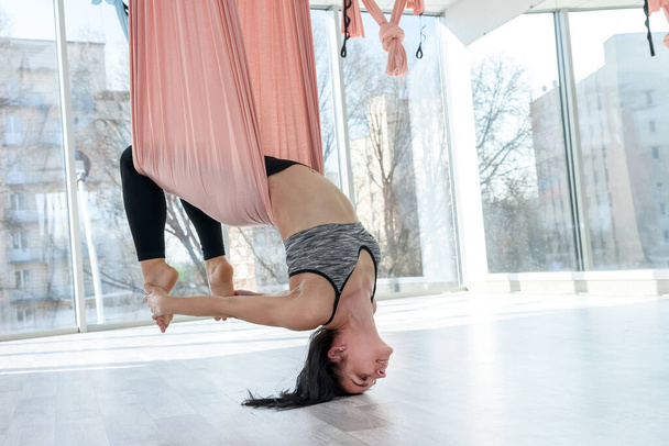 Ziemlich schlanke Frau praktiziert Antennen-Inversion-Antigravitations-Yoga mit einer Hängematte in einem Fitness-Studio. Balance im Lebensstil - Foto, Bild