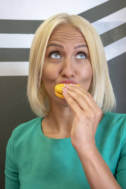 Een jonge vrouw van 25-30 jaar oud neemt een hap van een rond koekje en geniet ervan. Onderwerp: genot van snoep door vrouwen, licht ontbijt in een café. - Foto, afbeelding