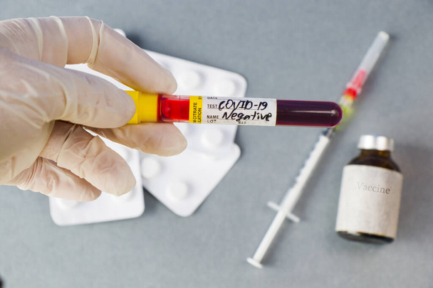 Коронавирус и Ковид - 19 отрицательных анализов крови у врачей в белых перчатках, ампулах от вакцины и игле на заднем плане - Фото, изображение