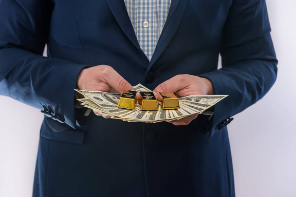 El hombre de traje tiene billetes de dólar y lingotes de oro. Éxito empresarial - Foto, imagen