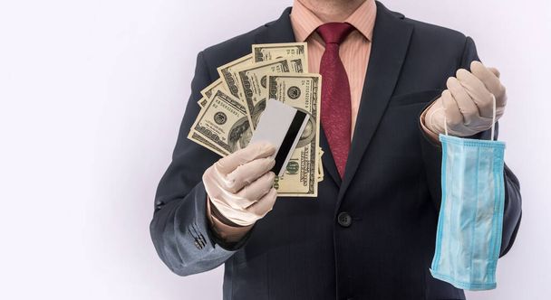 Чоловічі руки в медичних рукавичках тримають доларові банкноти та захисну медичну маску, безпеку ковадла19. криза
 - Фото, зображення