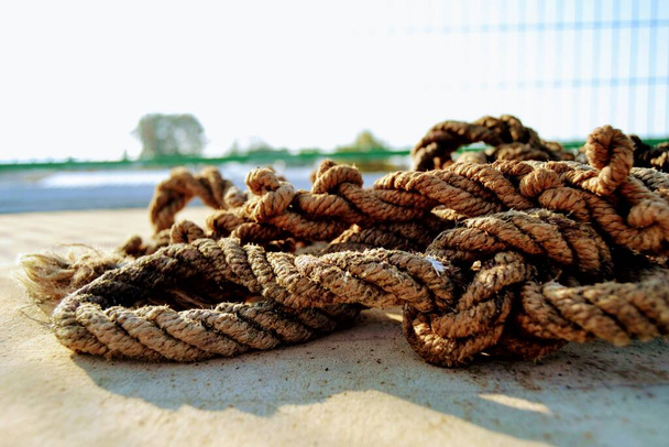 Una cuerda vieja y deshilachada parada en un lío. Vieja cuerda de pie en el suelo de hormigón y su sombra se muestra. - Foto, imagen