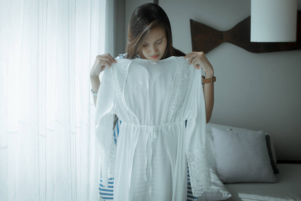 Mulher asiática experimentando um novo robe de cetim branco em casa. Uma menina acabou de comprar um novo laço de seda sexy nightwear - Foto, Imagem