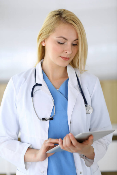 Doctor woman at work while standing straight in hospital or clinic. Blonde cheerful physician using tablet pc. Data and best service in medicine and healthcare - Фото, зображення