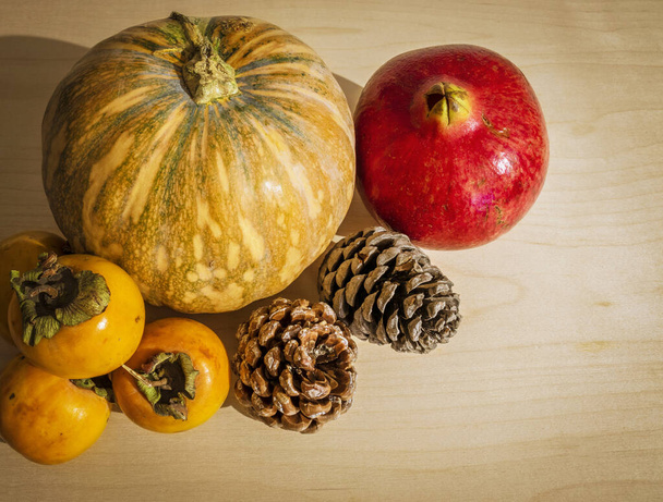 Winterfrüchte und -gemüse auf einem Holzboden. Granatapfel, Kürbis, Kaki und Tannenzapfen. Weihnachten und Winterferien. Nahaufnahme und weißer Hintergrund. - Foto, Bild