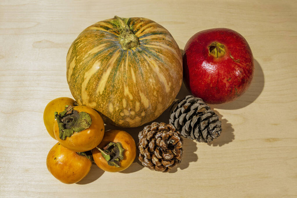 winterfruit en -groenten op een houten vloer. Granaatappel, pompoen, persimmon en dennenappels. Kerst- en wintervakantie. Close-up en witte achtergrond. - Foto, afbeelding