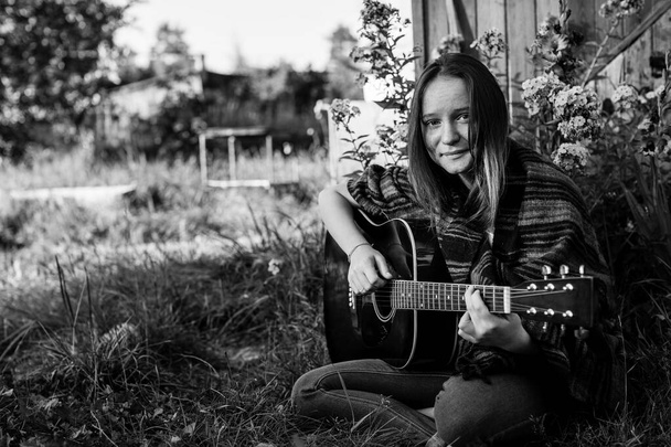 Giovane ragazza che suona la chitarra acustica seduta all'aperto. Fotografia in bianco e nero. - Foto, immagini