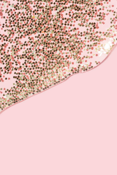 líquido transparente com brilho de ouro derramando sobre um fundo rosa pastel - Foto, Imagem