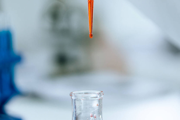 red liquid in a laboratory pipette on a blurry background. - 写真・画像