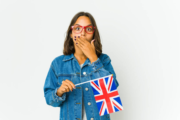 Młoda Latynoska kobieta trzymająca angielską flagę odizolowaną na białym tle zaszokowała usta dłońmi. - Zdjęcie, obraz