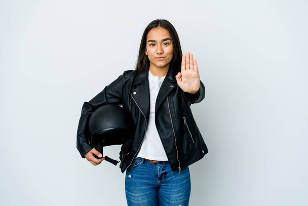 Joven mujer asiática sosteniendo un casco de moto sobre fondo aislado de pie con la mano extendida mostrando señal de stop, que le impide. - Foto, imagen