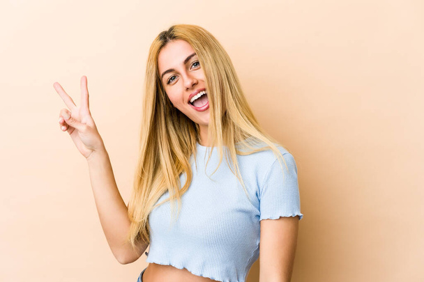 Young blonde caucasian woman joyful and carefree showing a peace symbol with fingers. - 写真・画像