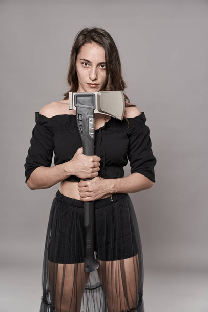 Menacing but hot woman holding a big axe on gray background - Foto, imagen