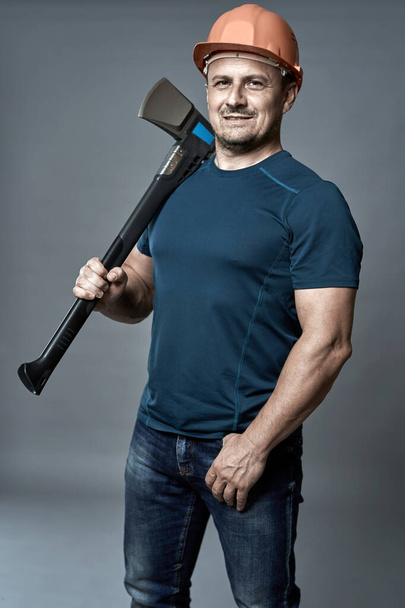 Portrait of a lumberjack in hardhat holding a big axe for splitting - Foto, afbeelding